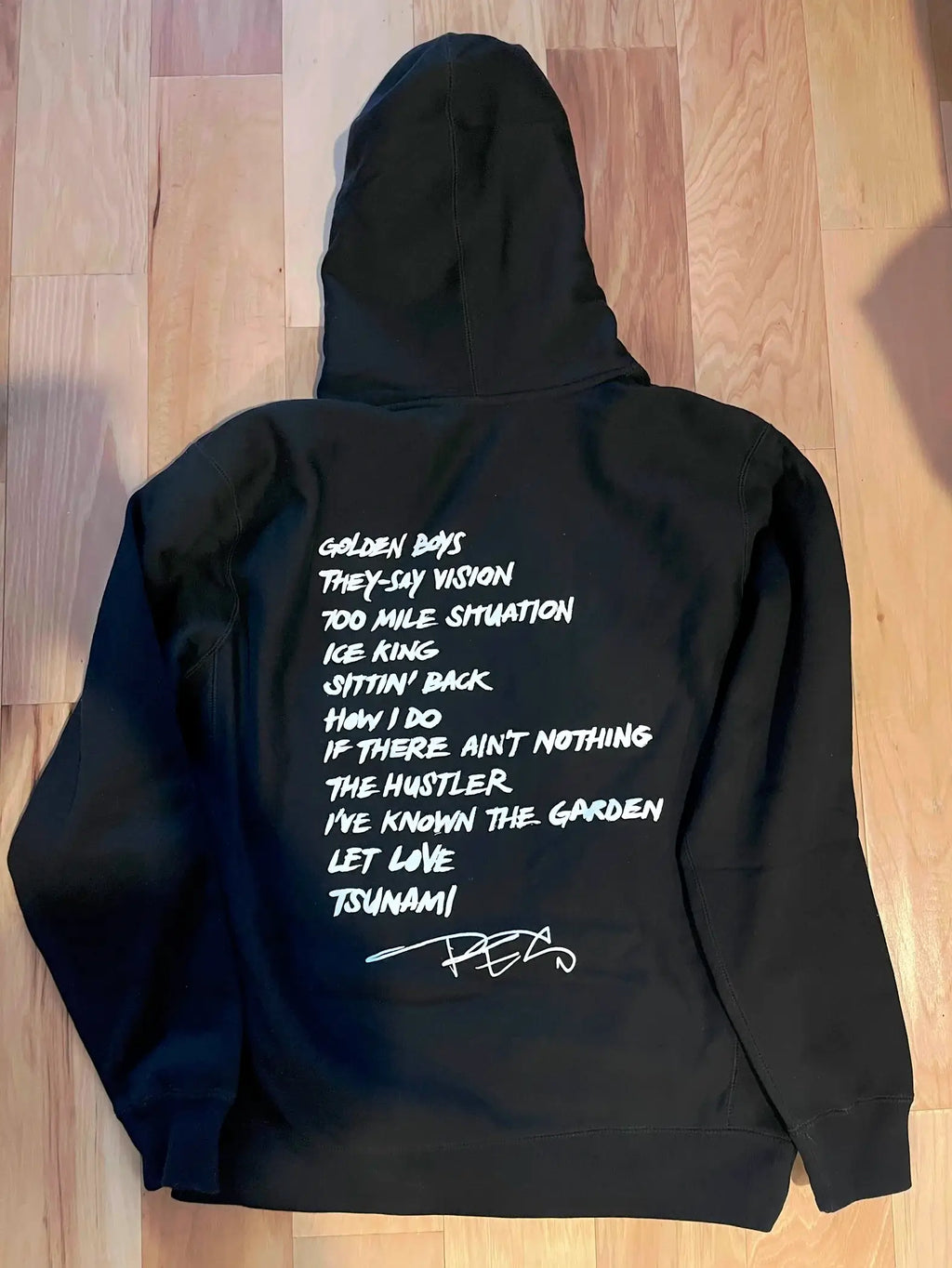 Black hoodie with how i do tracklisting in white text on the back on a wooden floor